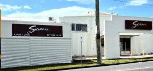 Refurbished Snooze store exterior with clean white walls and updated brown signage under a bright blue sky.